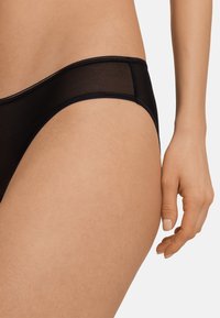 Bikini trasparente nera con una finitura liscia, caratterizzata da un design a vita bassa e un sottile elastico in vita.