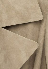 Primo piano di tessuto in pelle scamosciata beige piegato in forme rettangolari sovrapposte con una texture liscia e morbida e bordi arrotondati.