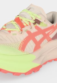 Chaussure de course beige et corail avec lacets jaune fluo, semelle avant jaune fluo, semelle extérieure corail et bandes latérales caractéristiques.
