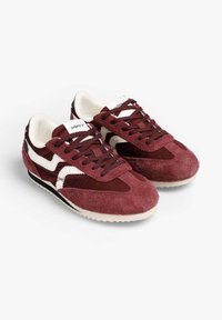 Zapatillas de ante burdeos con acentos en blanco, parte superior texturizada, punta redonda y suela de goma negra. Diseño con cordones y cuello acolchado.