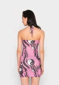 Vestido mini rosa sem alças com padrões yin-yang em preto e branco, apresentando um design justo e laços no pescoço. Tecido liso e elástico.