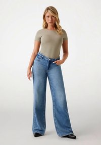 Verbleekte blauw gespreide jeans van denim, gecombineerd met een licht olijfgroen nauwsluitend shirt met korte mouwen. Voorzien van steekzakken aan de voorkant en een logo-detail.