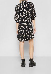 Černé šaty s květinovým vzorem v krémové barvě, mají nabírané rukávy, volánkový lem a vysoký límec. V kombinaci s černými robustními kotníkovými botami.