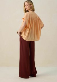 Blouse en georgette pêche à manches courtes et détails froncés au dos, associée à un pantalon large bordeaux. Tissu lisse et coupe décontractée.