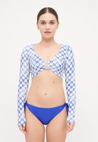 Long-sleeved bikini top with a floral pattern in blue and yellow, featuring a v-neck and ruched detail. Paired with solid blue bikini bottoms.