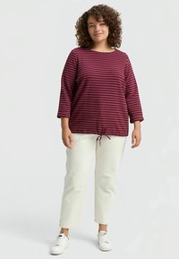 Langærmet top med brede striber i bordeaux og mørk rosa, rund halsudskæring og justerbar snøre i kanten, kombineret med hvide bukser og sneakers.