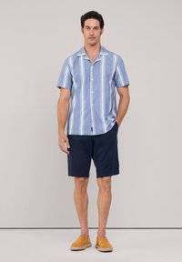 Camisa de botones de manga corta, color azul claro, con rayas verticales blancas, combinada con pantalones cortos azul marino y zapatos de lona color beige.