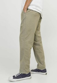 Khakifarbene Baumwollhose mit Seitentaschen, geradem Schnitt und sichtbaren Nähdetails. Getragen mit navy blauen Sneakers mit weißen Akzenten.
