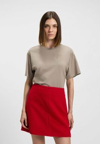 T-shirt en coton beige à manches courtes avec un "H" brodé sur la poitrine, associé à une mini-jupe texturée rouge vif.