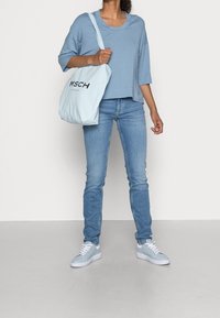 Top corto azzurro, jeans in denim azzurro e sneakers azzurri chiari. La borsa presenta un testo nero su un tessuto morbido. Outfit informale.