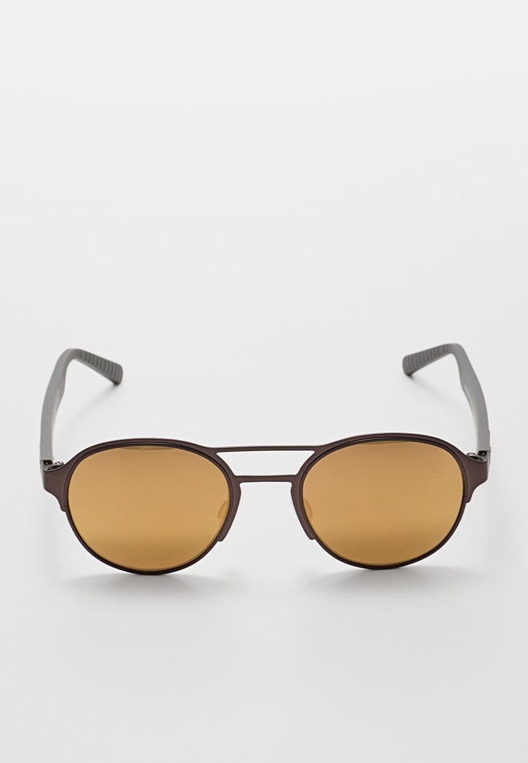 Gafas de sol marrones en forma ovalada con lentes tintados y un marco delgado y oscuro. Las patillas cuentan con un agarre texturizado para mayor comodidad y estabilidad.