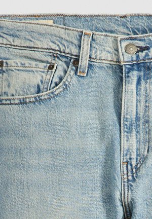 Jeans de mezclilla azul claro con un diseño clásico de cinco bolsillos, que presentan herrajes de cobre, costuras en tono y una textura suave, ligeramente desgastada.