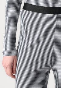 Bodysuit rayé noir et blanc à manches longues, avec une taille noire et une texture côtelée. Gros plan sur le tissu et une main tenant le matériau.