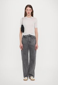 Top corto de manga corta blanco con canalé y logo en el cuello, combinado con pantalones vaqueros negros de cintura alta y un pequeño bolso de mano negro con lentejuelas.