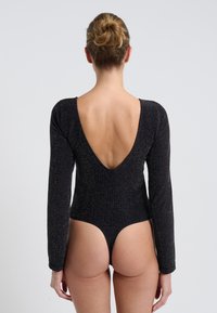 Czarny bodysuit z długim rękawem, z niskim wycięciem na plecach, wykonany z teksturowanej tkaniny o subtelnym połysku. Wysokie wycięcia nogawek.