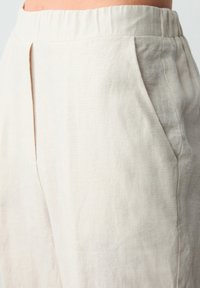Pantaloni in lino beige con vita elastica, tasche laterali e una texture liscia, caratterizzati da una vestibilità rilassata e dettagli delle cuciture sottili.