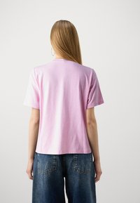 Light pink cotton t-shirt with short sleeves, round neckline, and an unembellished back, paired with relaxed-fit blue denim pants.