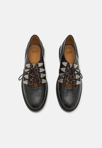 Mustad mustreeritud mustad nahkkingad, millel on dekoratiivsed tiivakujulised aktsendid paeltel, brogue-detailid ja tugev tald. Siseosa on tan värvi voodriga.