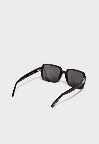 Lunettes de soleil noires rectangulaires avec des verres foncés. Matériau en plastique brillant, design minimaliste. Présente un logo sur le côté de la branche.