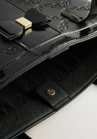 Borsa a mano in pelle verniciata nera con motivo impresso, dotata di un fiocco decorativo e hardware dorato. Interno foderato in un tessuto nero testurizzato.