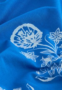Blauwe stof met witte bloempatronen heeft een gladde textuur. Het ontwerp omvat gestileerde bloemen en bladeren in verschillende groottes.