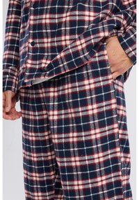 Red, white, and navy plaid flannel pajama set with a button-up top and elastic waistband pants, showcasing a soft texture and relaxed fit.