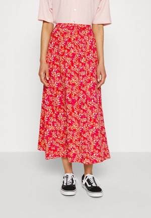 Personne portant une jupe rose mi-longue avec des motifs de feuilles orange, des baskets noires et blanches, et une chemise à manches courtes rose pâle boutonnée.