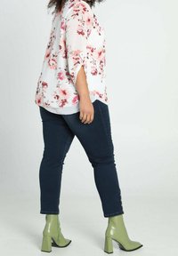 Blusa bianca leggera con motivo floreale e maniche corte; abbinata a jeans skinny scuri e stivaletti verde lucido con tacco a blocco.