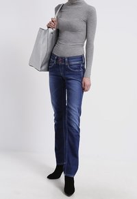 Gray ribbed turtleneck, blue denim jeans with five pockets, and black heeled ankle boots. Carrying a textured gray handbag.