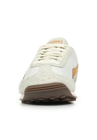 Sneaker atletica bianca con una parte superiore in crema texturizzata, suola in gomma marrone e dettagli in pelle. Presenta un design con lacci e linguetta imbottita.
