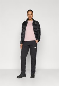 Μαύρο μονωμένο μπουφάν, ανοιχτό ροζ μπλουζάκι, μαύρο παντελόνι. Το μπουφάν έχει κεντητό σχέδιο· λογότυπο στο μπλουζάκι και στο παντελόνι. Τα παπούτσια είναι μαύρα.