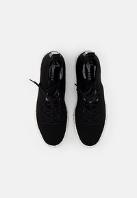 Černé pletené tenisky s texturovaným svrškem, zaoblenou špičkou a kontrastníma skvrnitýma bílýma podrážkama. Černé tkaničky a logo na jazyku dotvářejí design.