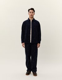 Completo in velluto a coste navy composto da una camicia con bottoni e pantaloni abbinati con sottili punti a fantasia, completato da una maglia crema e scarpe marroni.