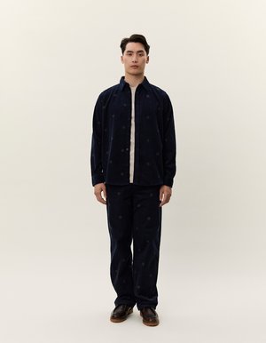 Námořnický kordový outfit obsahující košili na knoflíky a odpovídající kalhoty s jemnými vzorovanými tečkami, doplněné krémovým tričkem a hnědými botami.