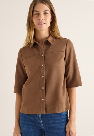 Chemise en suede marron à manches courtes, col pointu et devant à boutons. Présente une texture lisse et des surpiqûres discrètes.