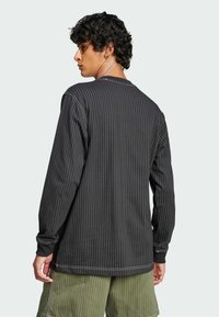 Black long-sleeve shirt with vertical white stripes, featuring a round neckline and ribbed cuffs, paired with green shorts.