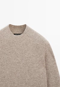 Beige strikket sweater med høj hals, ribbet tekstur og skuldersømme. Blødt stof med et ensartet mønster hele vejen igennem.