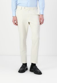 Helle beige maßgeschneiderte Hose aus glattem Stoff, mit flachem Frontschnitt, schlanker Passform und Seitentaschen, kombiniert mit schwarzen Mokassins.