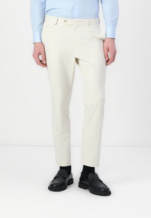Light beige tailored trousers made of smooth fabric, featuring a flat front, slim fit, and side pockets, paired with black loafers.
