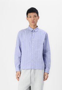 Light blue striped shirt with white splatter pattern, button-up front, long sleeves, and a collar, paired with gray sweatpants.