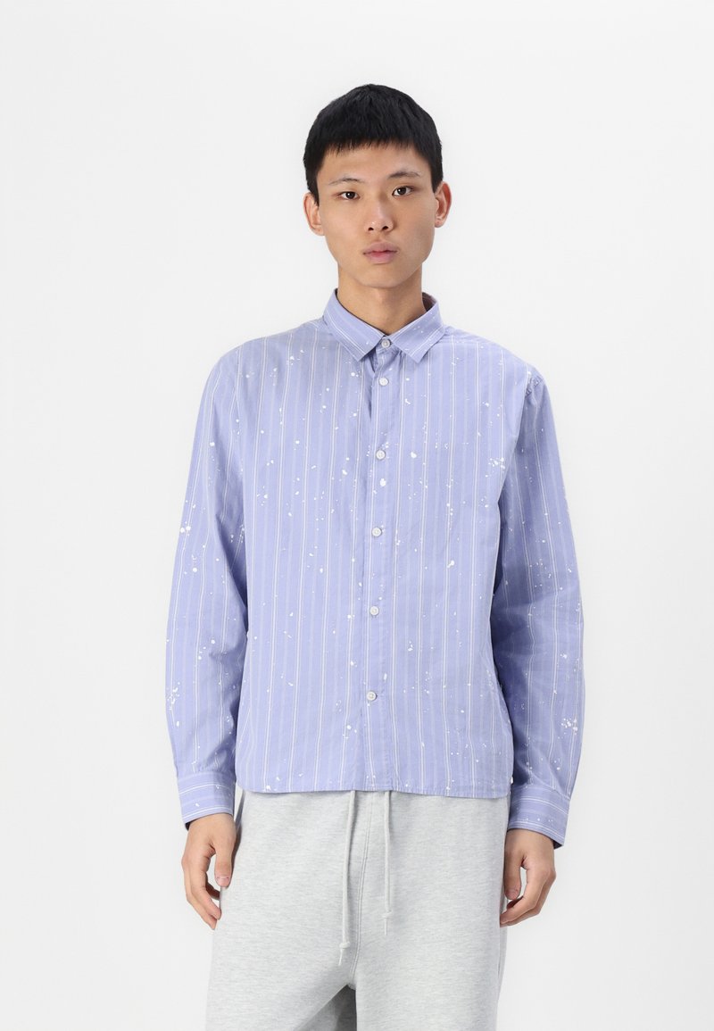 Light blue striped shirt with white splatter pattern, button-up front, long sleeves, and a collar, paired with gray sweatpants.