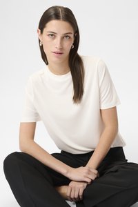 Hvid kortærmet t-shirt med rund hals, glat tekstur, båret med løse sorte bukser. Klare og ensartede stikninger som konturer.