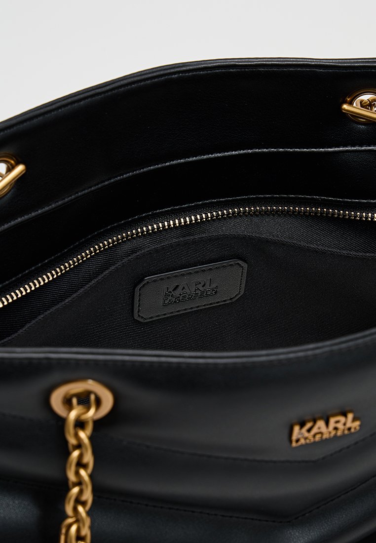 Interior de bolso de cuero negro con herrajes dorados, que incluye un bolsillo con cremallera y una etiqueta con el logo. El forro texturizado aporta contraste.