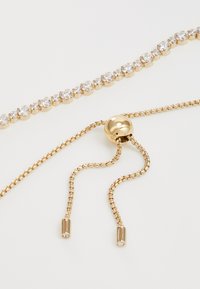 Goldene Kettenarmband mit klaren, runden Strasssteinen, die in einer Krappenfassung eingesetzt sind, mit einem gleitenden verstellbaren Verschluss und feinen Kettendetails.