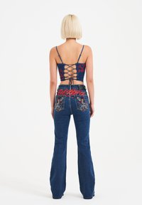 Denim crop top med blåt stof og røde broderede mønstre; parret med flagrende blå jeans med dekorative baglommer og detaljer på taljen.