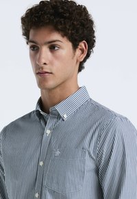 Overhemd met knopen, voorzien van marineblauw en witte verticale strepen, een klassieke kraag en een borstzak met geborduurd detail. Katoenen stoftextuur.