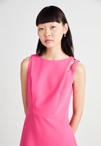 Fuchsia sleeveless dress with a round neckline and cutout shoulder details. Smooth, textured fabric with a fitted silhouette.