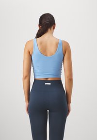 Top estivo blu a spalla corta con scollatura rotonda, abbinato a leggings blu scuro a vita alta con un cinturino testurizzato e dettagli del logo.
