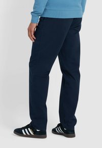 Navyblauwe broek gemaakt van een gladde stof, met rechte pijpen en zijzakken. Gemaakt met zwarte sneakers met witte strepen.