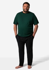Grönrandig t-shirt med kort ärm, i kombination med svarta byxor. T-shirten har en avslappnad passform och en mjuk textur. Modellen står med händerna i fickorna.